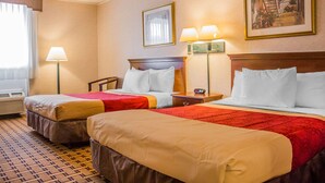 A hotel room with two beds, a window with curtains, a painting on the wall, and a lamp on the nightstand. - Rodeway Inn Mystic (Mystic)