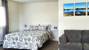Un dormitorio con una cama, un sofá gris y tres cuadros de paisajes en la pared.