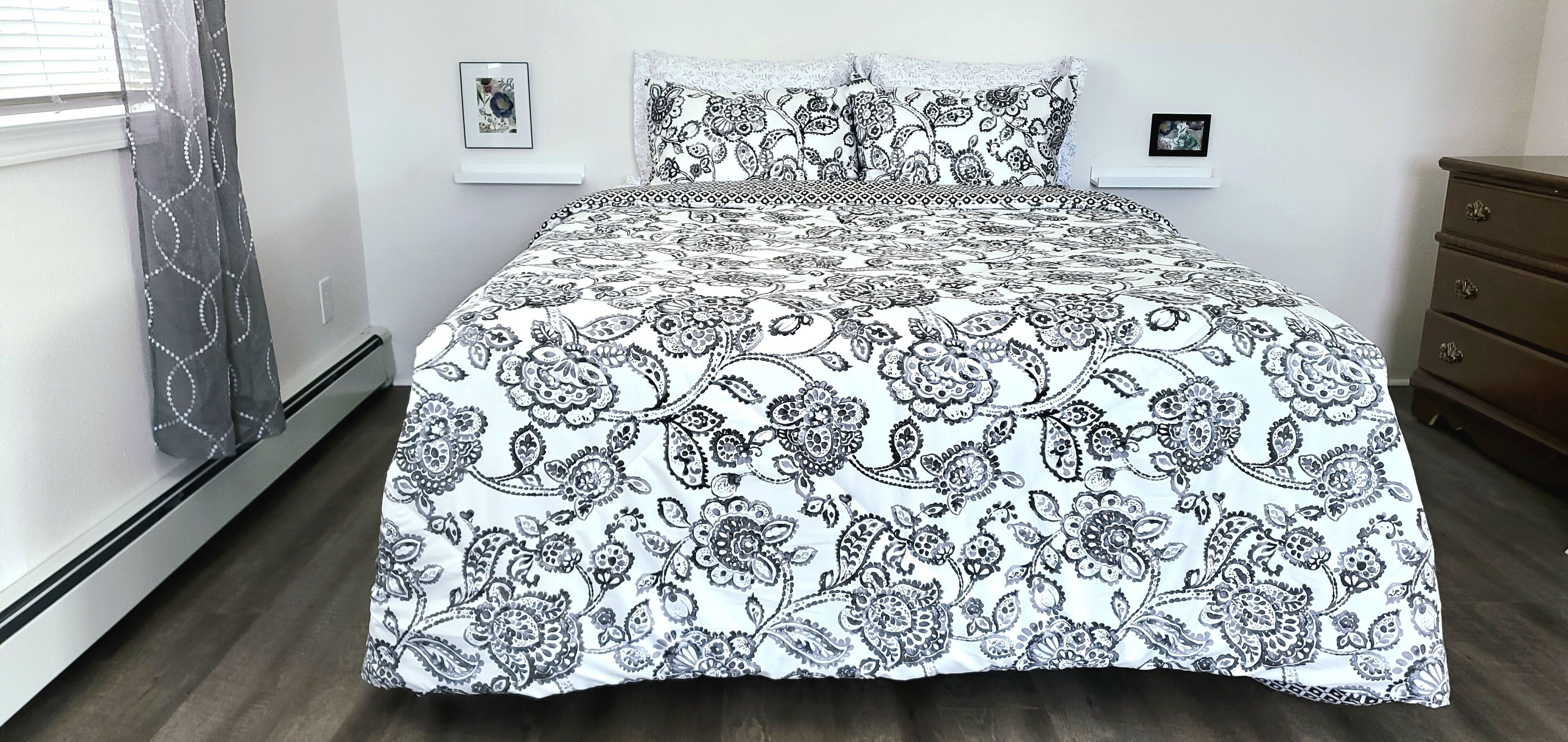 A bed with a patterned bedspread and matching pillows, a dresser, and two framed pictures on the wall.