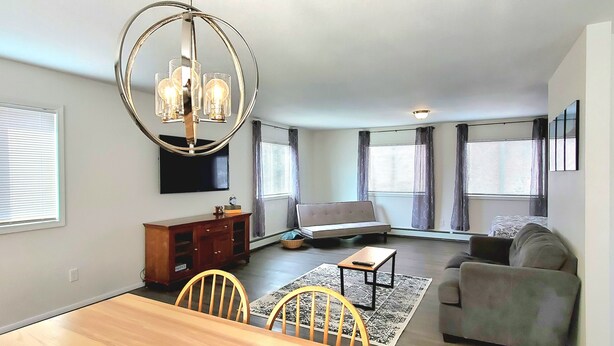 Una sala moderna con una mesa de comedor de madera, dos sillas, un sofá, un sillón y una gran lámpara de araña circular.