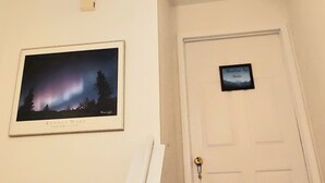 Un pasillo con una puerta blanca, un cuadro enmarcado de la aurora boreal y tres lámparas colgantes.