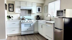 Una cocina con armarios blancos, estufa, microondas y refrigerador.