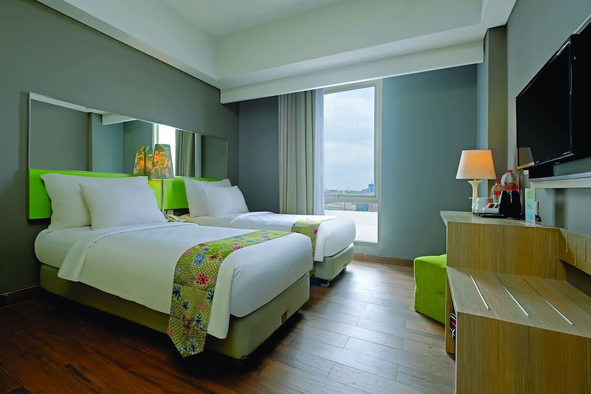 A hotel room with two beds, a desk, a television, and a large window.