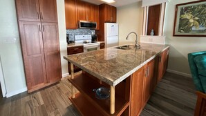 A modern kitchen with wooden cabinets, a granite countertop, stainless steel appliances, and a tiled backsplash. - Private Oceanfront Top Floor Condo - Kona Reef D34 (Kailua-Kona)