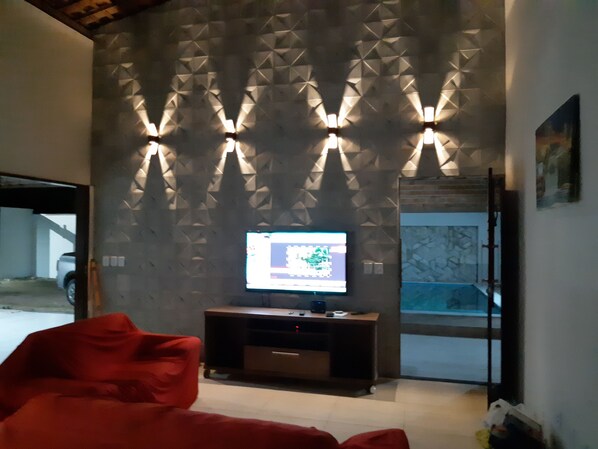 A modern living room with a geometric wall design, a flat-screen TV on a wooden stand, and a red sofa.