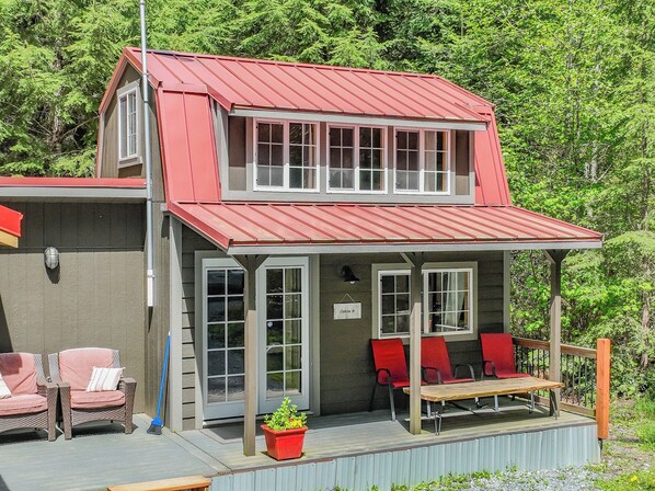 A two-story building with a red roof, a covered porch with red chairs, and a sign indicating 'Cabin B'. - Tiny Cabin B, Steps from Mt. Rainier Nat Park W/ firepit close to river & trails (Ashford)