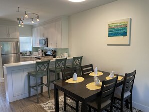 A modern kitchen with white cabinets, a dining area with a dark wooden table and chairs, and a painting on the wall.
