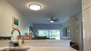 A modern kitchen with a dishwasher, a ceiling fan, and a large window providing a view of the outdoors. - 7Mile Pool/Seaside Bliss - 2bed 2bath Ground Suite (George Town)