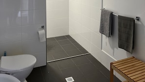 Ein modernes Badezimmer mit weißen Fliesen, einer Glasdusche, einer Holzbank und einem Handtuchhalter mit zwei Handtüchern.