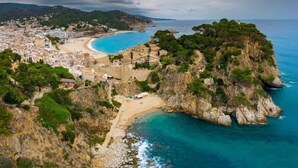 Vue aérienne d’une ville côtière avec une plage, des falaises rocheuses et une fortification historique.