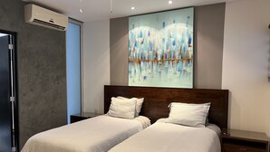 A bedroom with two beds, a ceiling fan, an air conditioning unit, and a large abstract painting on the wall. - Perfect location in Playa! (Playa del Carmen)