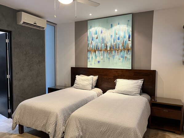 A bedroom with two beds, a ceiling fan, an air conditioning unit, and a large abstract painting on the wall.