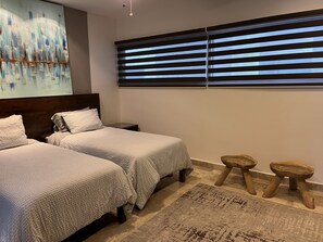 A bedroom with two beds, a nightstand, a window with blinds, a painting on the wall, and a rug.