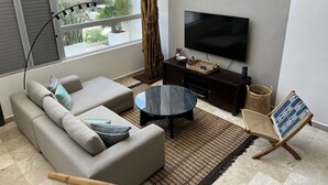 A modern living room with a sofa, a coffee table, a TV, and a wicker chair. - Perfect location in Playa! (Playa del Carmen)