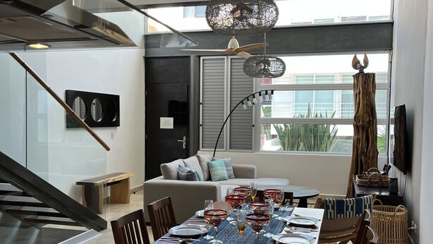 A modern kitchen with a granite countertop, a dining area with a table set for six, and a living area with a sofa and a TV. - Perfect location in Playa! (Playa del Carmen)