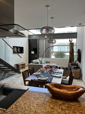 A modern kitchen with a granite countertop, a dining area with a table set for six, and a living area with a sofa and a TV. - Perfect location in Playa! (Playa del Carmen)