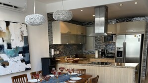 A modern kitchen with a central island, stainless steel appliances, and a dining area with a wooden table and chairs. - Perfect location in Playa! (Playa del Carmen)