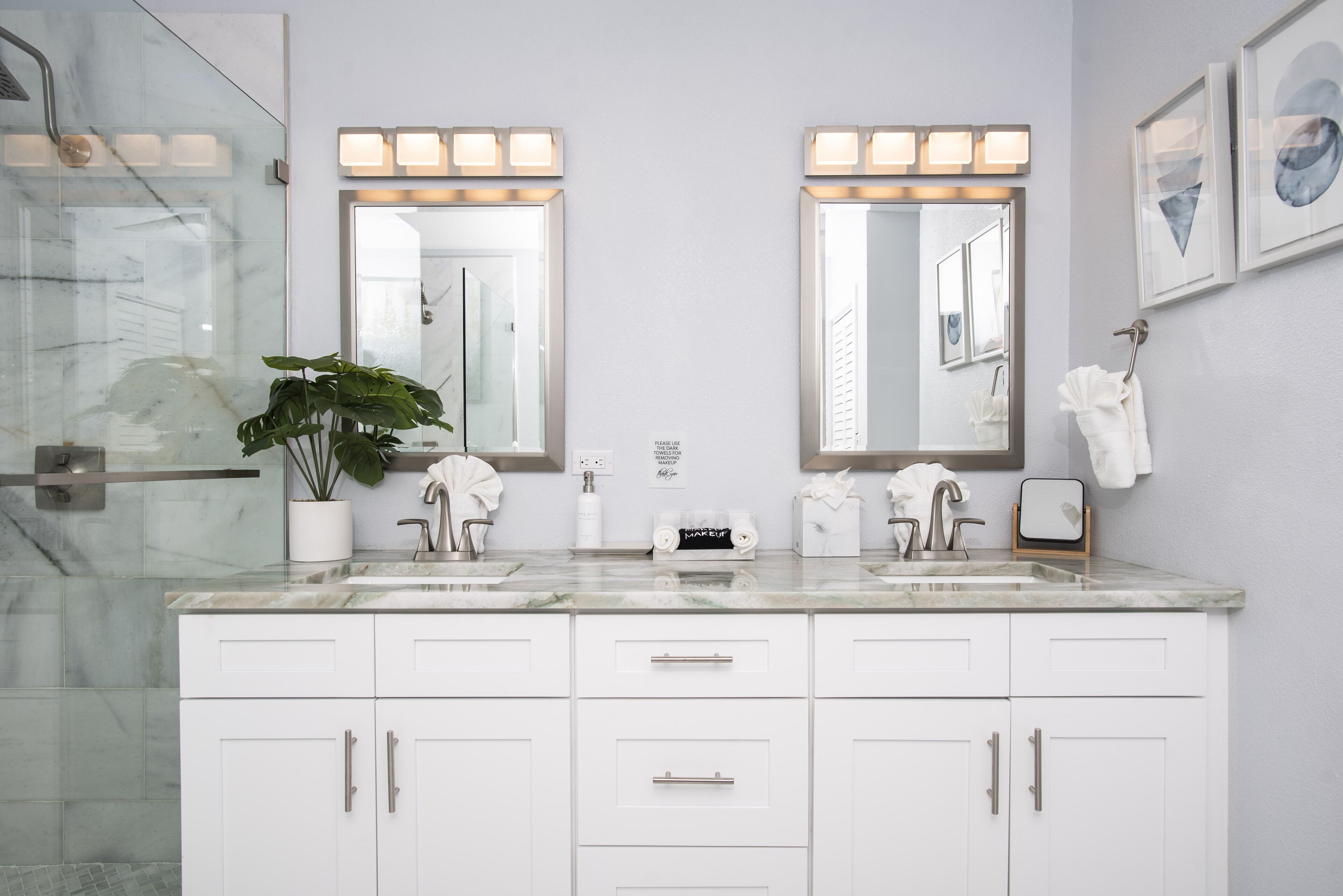 A bathroom with two sinks, a large mirror, and a potted plant.