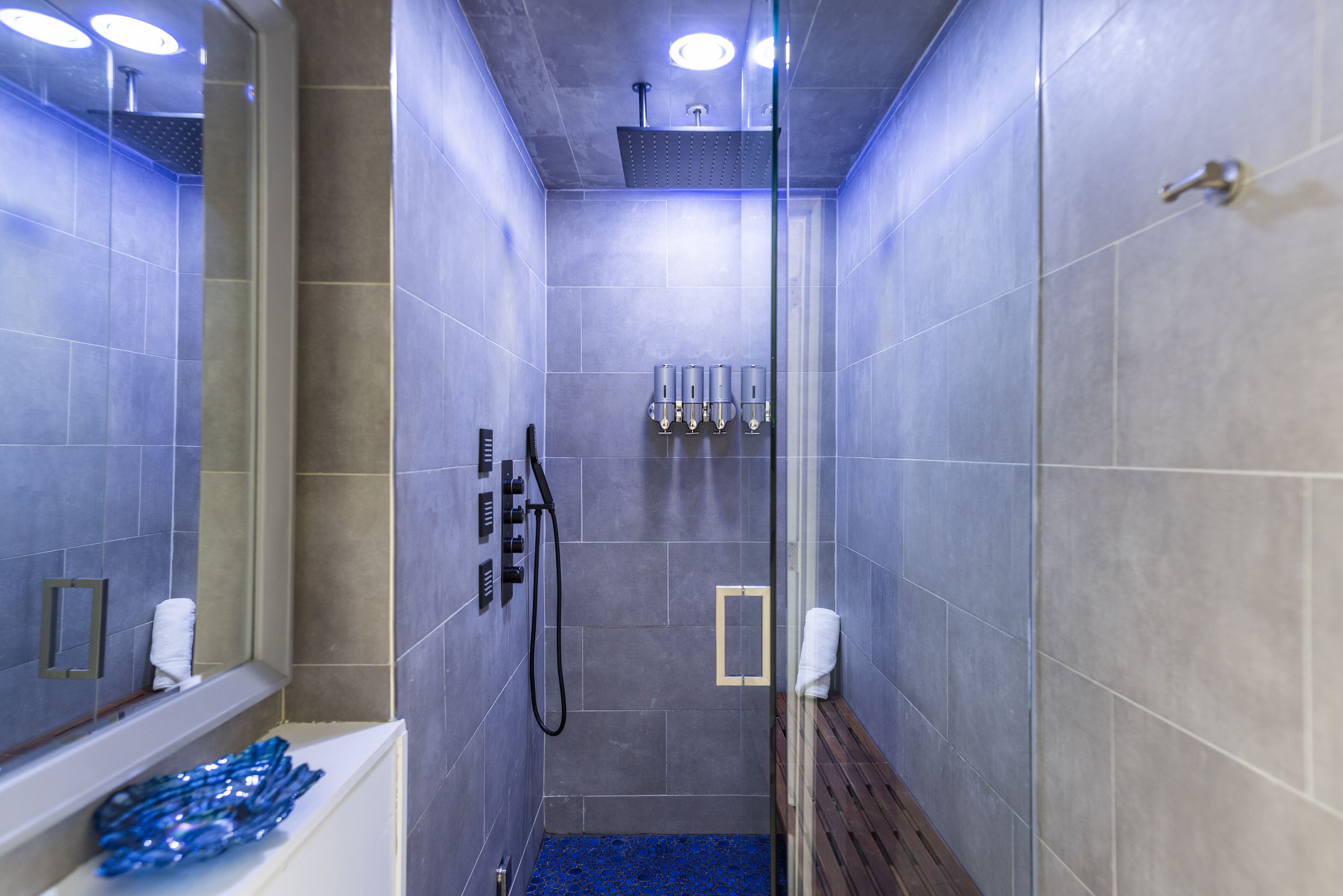 Un baño moderno con baldosas grises, zona de ducha, bañera y un banco.