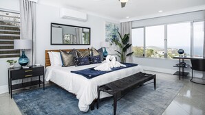 A modern bedroom with a large bed, a bedside table, a desk, and a view of the city. - 3 Villas,One Price/ Sleeps 16/ Steam Room/Private Pool/Close to everything Gated (St Thomas)