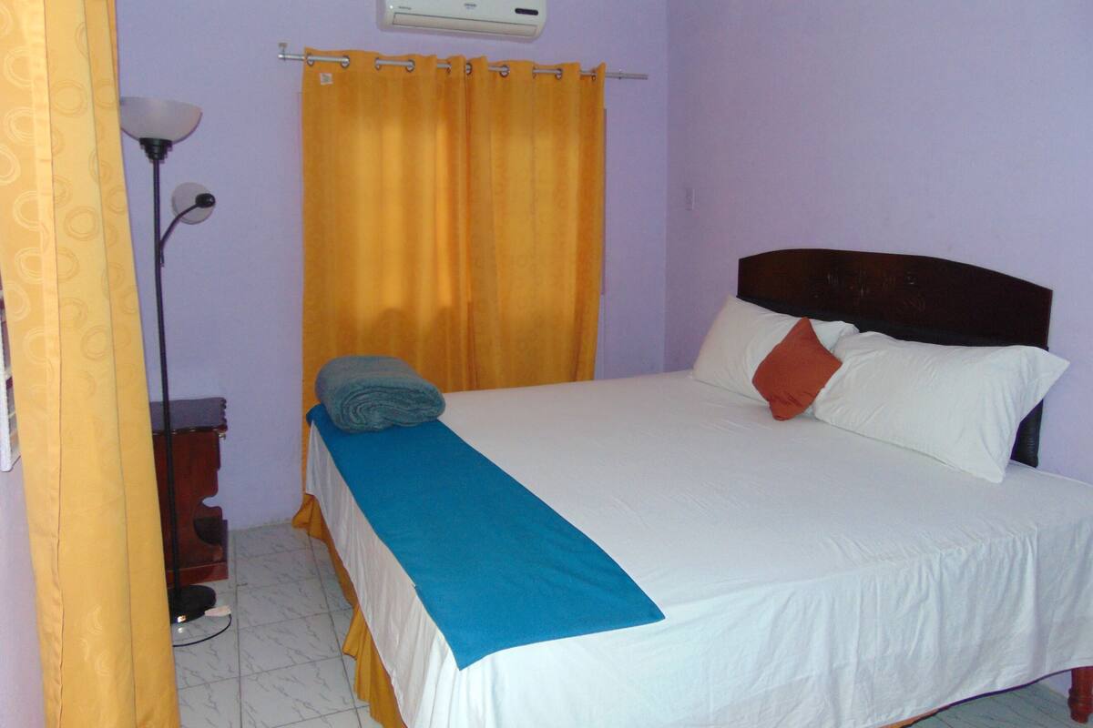 A bedroom with a bed, a nightstand, a lamp, and a curtain.