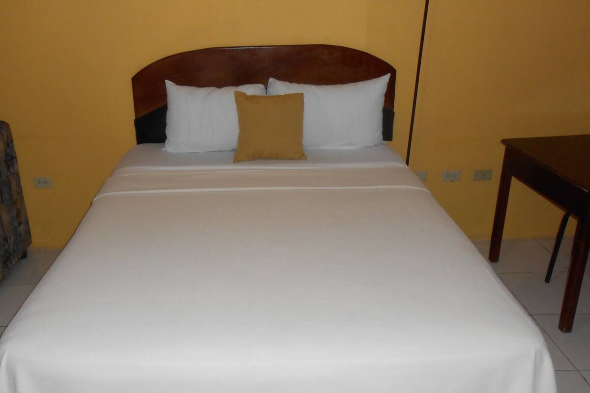 A bed with a wooden headboard, white bedding, and a single brown pillow.