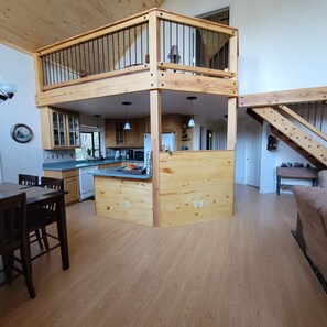 Open-plan living area with a central island, wooden cabinetry, and a staircase leading to an upper level.