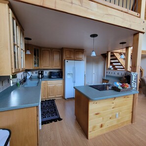 Kitchen features a microwave, refrigerator, and coffee maker, with a central island and pendant lights.