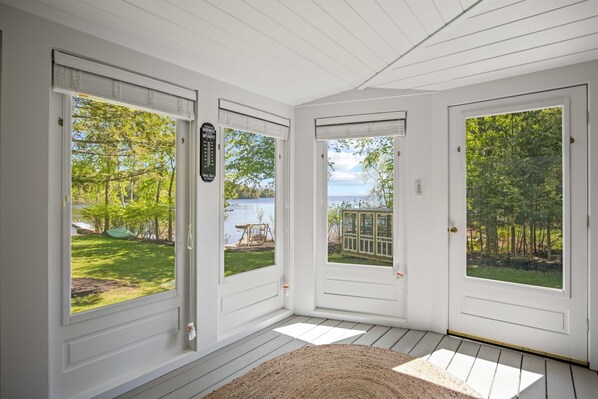 A room with three white doors leading to a deck with a view of a lake and trees.