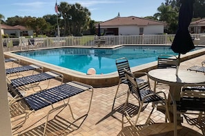 A swimming pool with lounge chairs and a table, surrounded by a fence and palm trees. - Walk to Beach & Fun! Heated Pool, Steps from Pool (Sarasota)