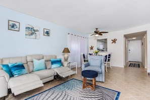 A living room with a sofa, a coffee table, and a chair. There are wall art pieces and a ceiling fan. - Walk to Beach & Fun! Heated Pool, Steps from Pool (Sarasota)