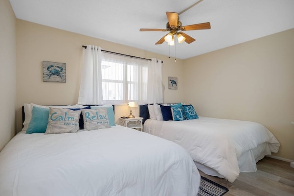 A bedroom with two beds, a ceiling fan, and a window with curtains.