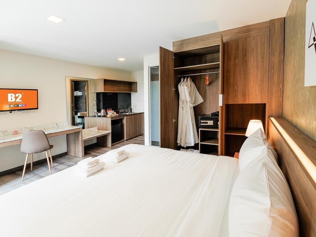 Quarto de hotel com cama, escrivaninha, cozinha compacta e armário.