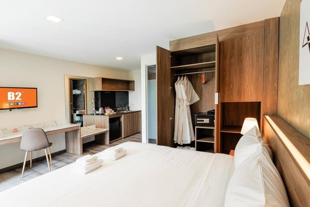 Quarto de hotel com cama, escrivaninha, cozinha compacta e armário.