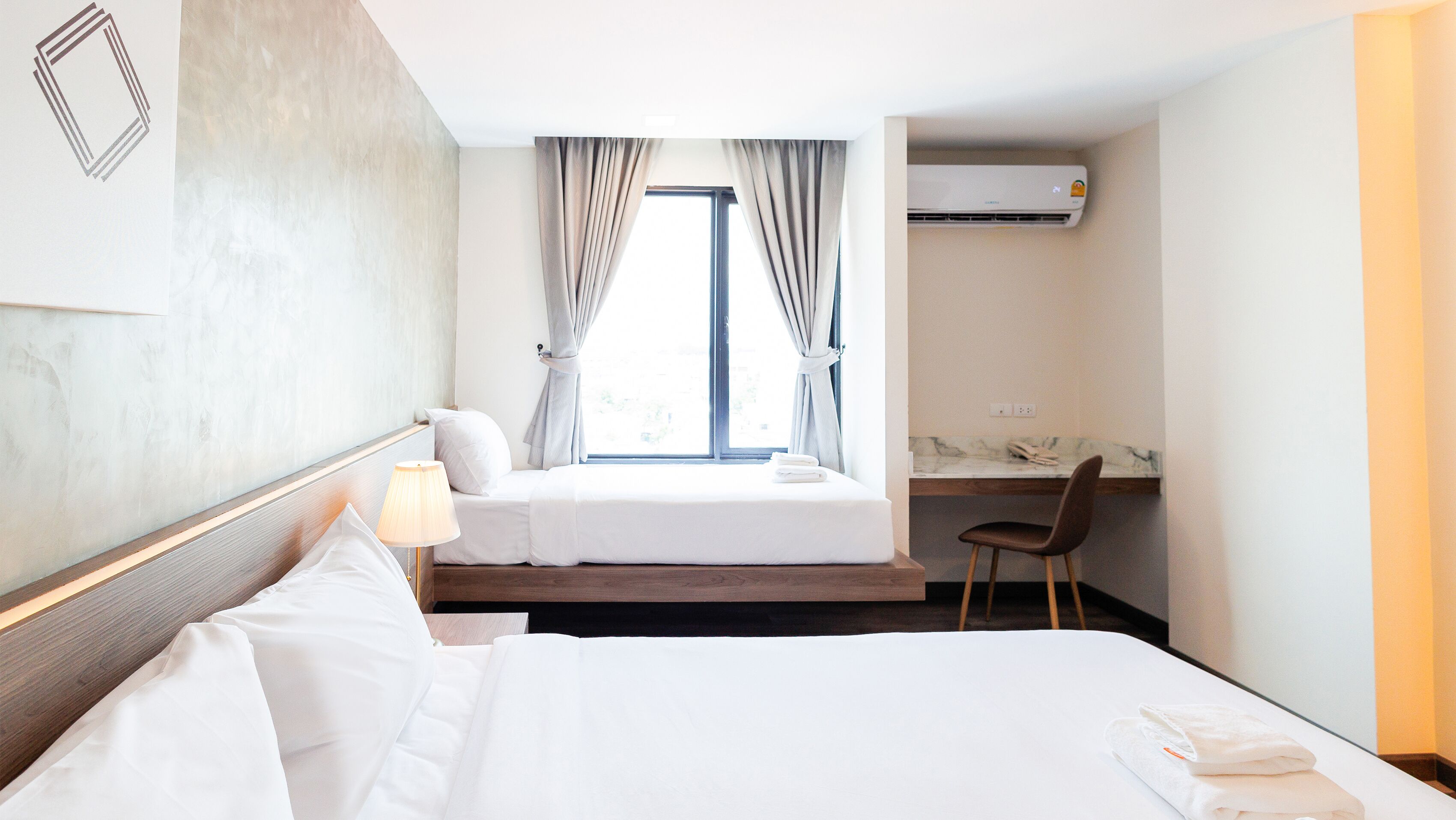 A hotel room with two beds, a desk, an air conditioning unit, and a view of the outdoors.