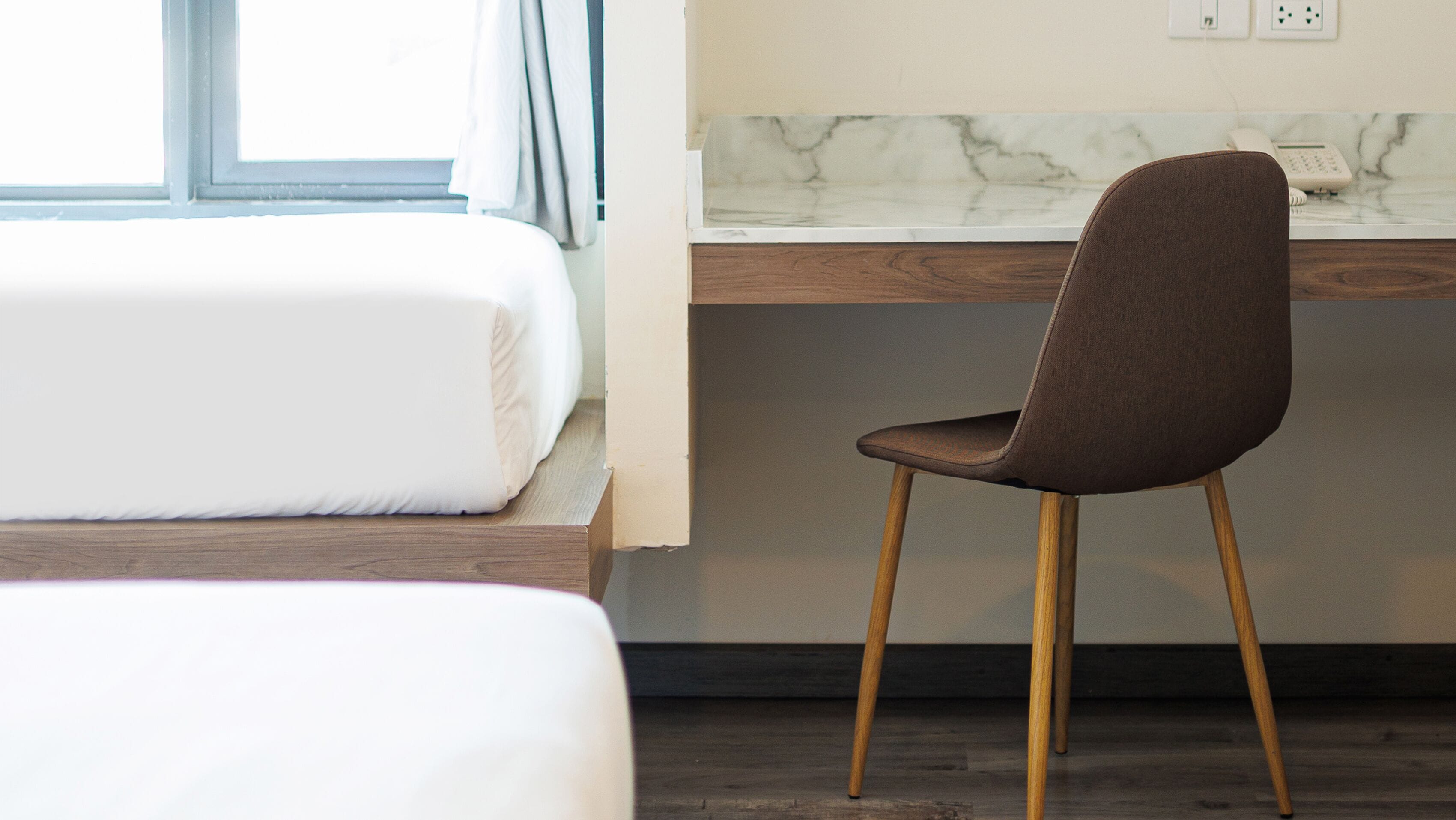 A hotel room with a bed, a desk with a chair, and a marble countertop.