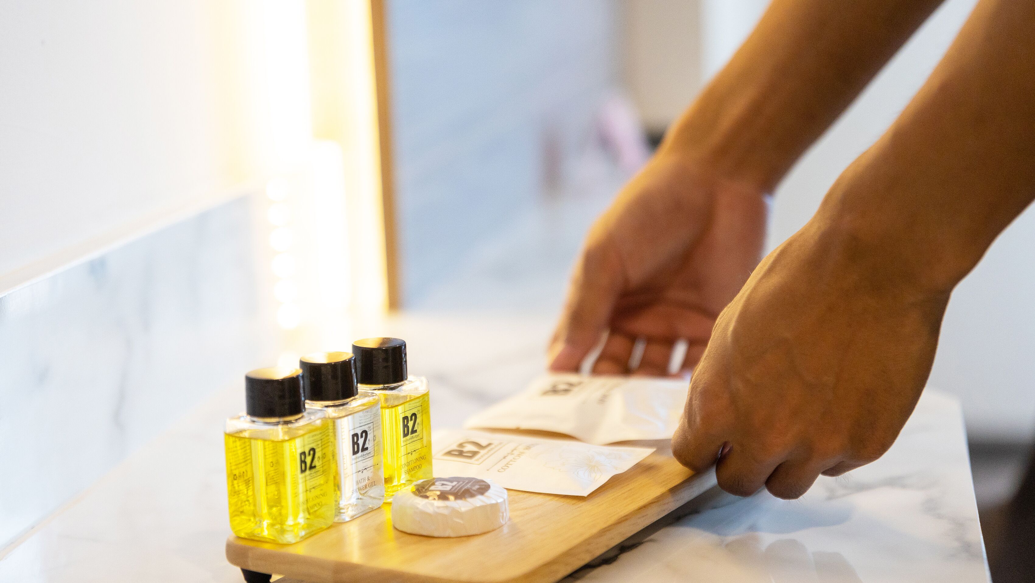 A wooden tray with three bottles of B2 bath and shower gel, a round soap, and a small white object on a marble surface.