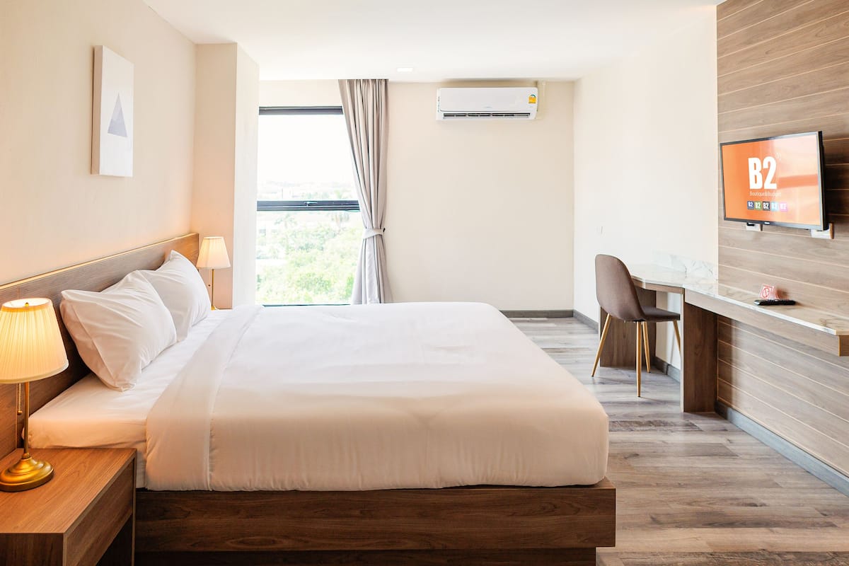 Une chambre d’hôtel équipée d’un lit, d’une table de chevet, d’une lampe, d’une télévision, d’un bureau, d’une chaise et d’un appareil de climatisation.