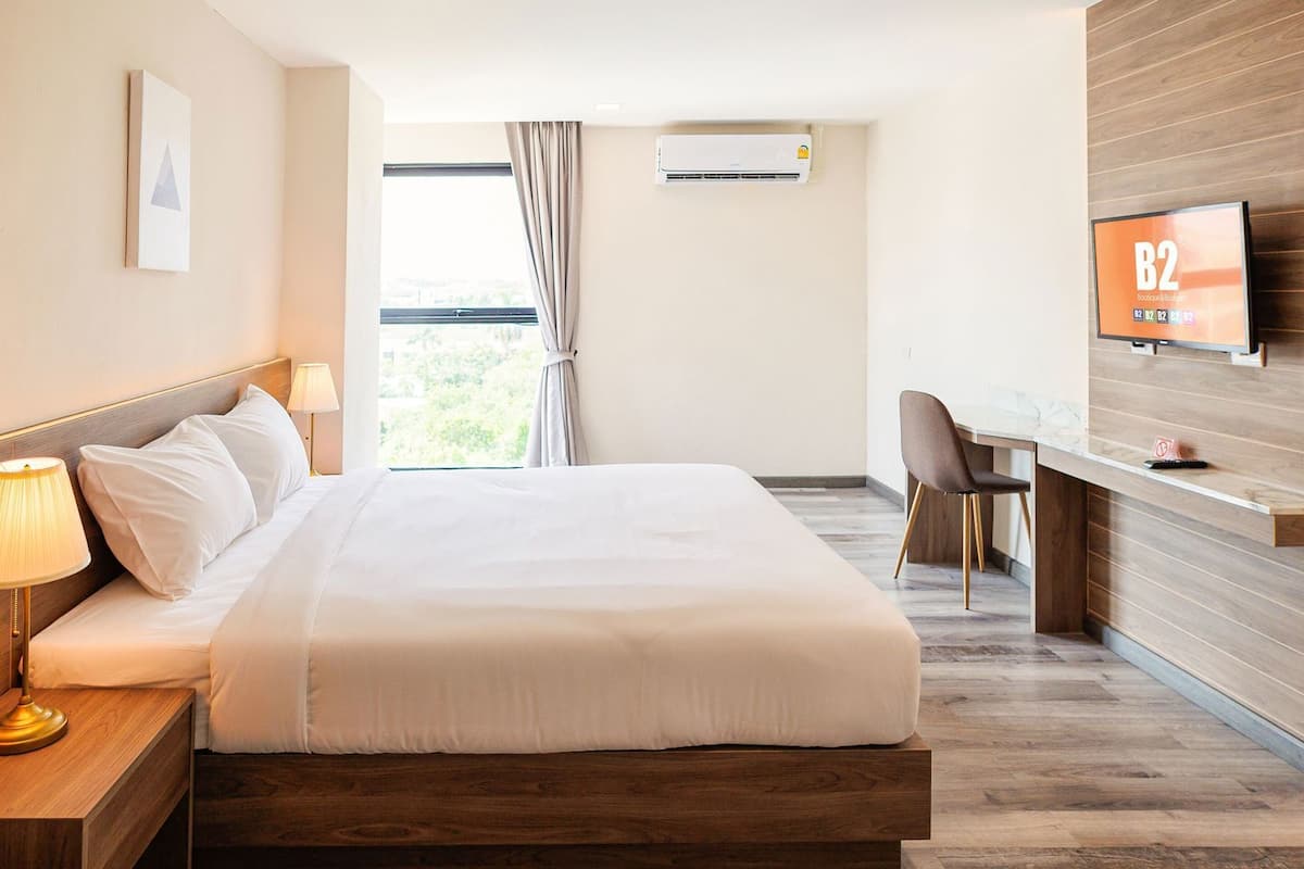 Une chambre d’hôtel comprenant un lit, une table de chevet, une lampe, un appareil de climatisation, une télévision, un bureau, une chaise et une vue sur la verdure.