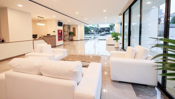 A modern lobby with white sofas, a reception desk, and a large glass window offering a view of the street. - B2 Khon Kaen Premier Hotel (Khon Kaen)