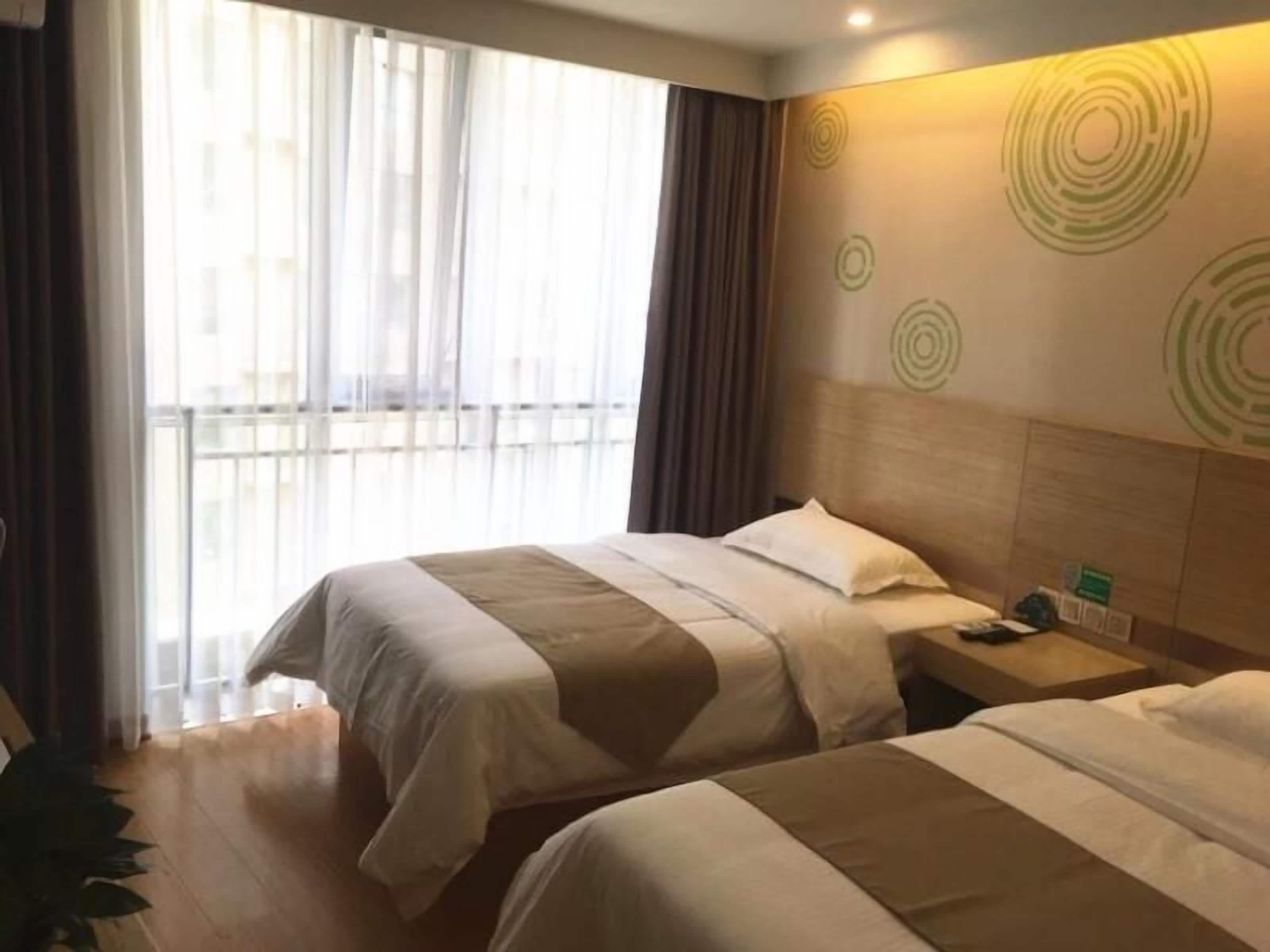 Ein Hotelzimmer mit zwei Betten, Holzboden, einem großen Fenster mit Vorhängen und einer Wand mit kreisförmigem Muster.