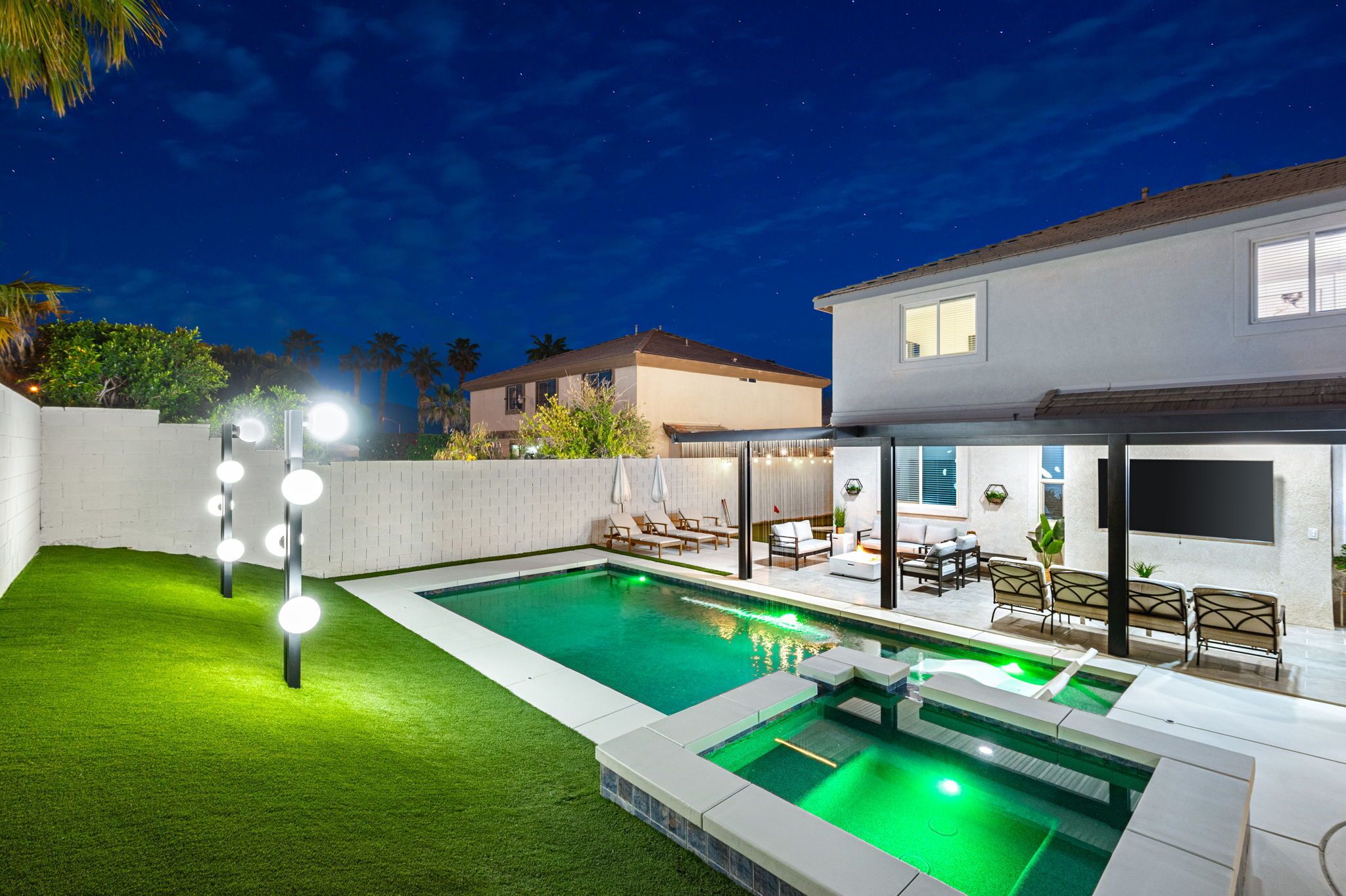 Ein modernes Haus mit Swimmingpool, Sitzgelegenheiten im Freien und einer gut beleuchteten Terrasse.