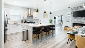 Una cucina moderna con mobili bianchi, un'isola centrale con sgabelli da bar e illuminazione a sospensione.