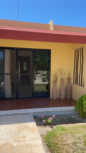 A building with a yellow facade, a red roof, and a sliding glass door leading to a patio area. There are three large vases with plants on the patio wall. - Beautiful beachfront loft in Celestun (Celestún)