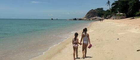 Una playa arenosa con agua cristalina y un promontorio rocoso al fondo.
