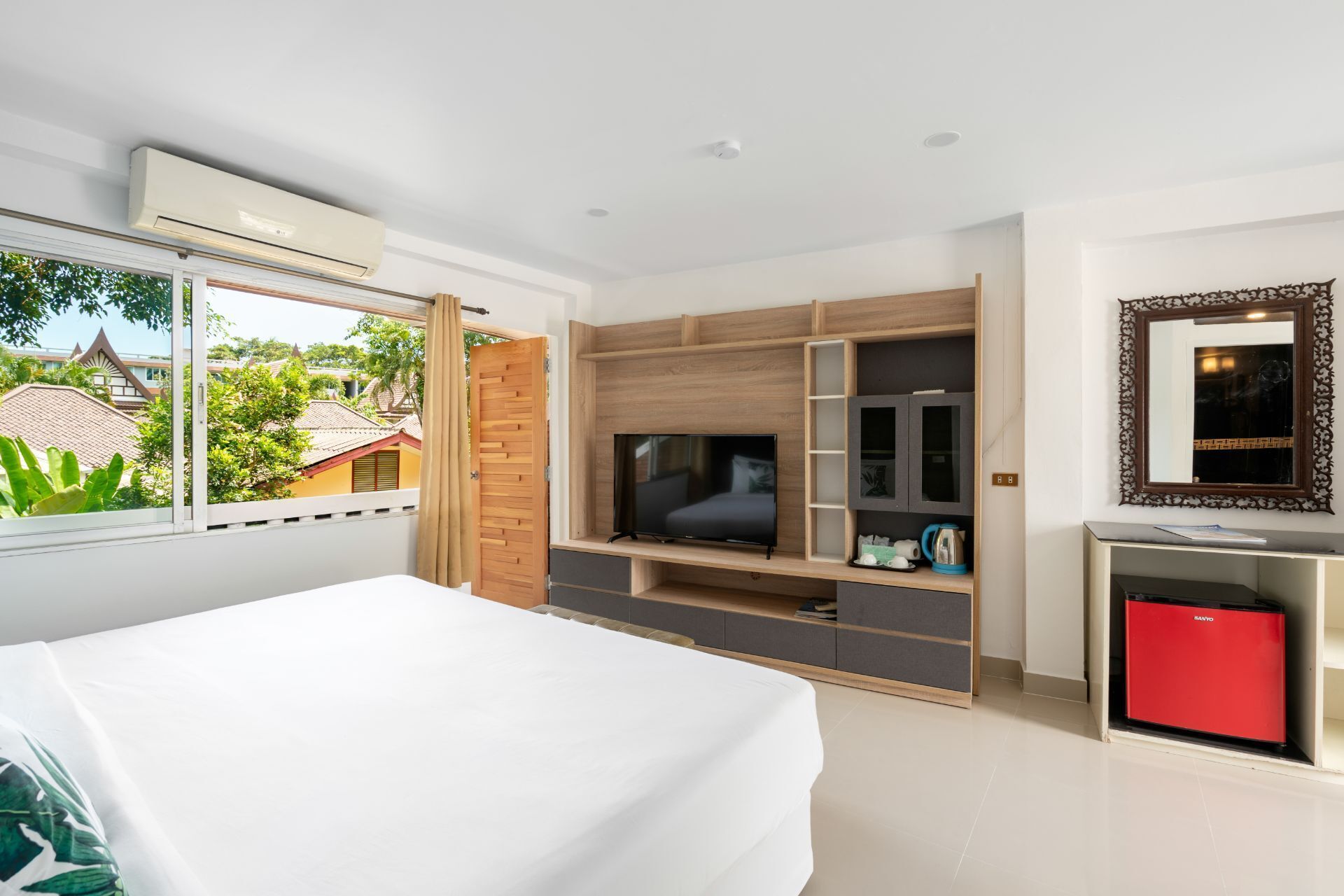 A modern hotel room with a large bed, a TV, a red minibar, and a view of the outside.