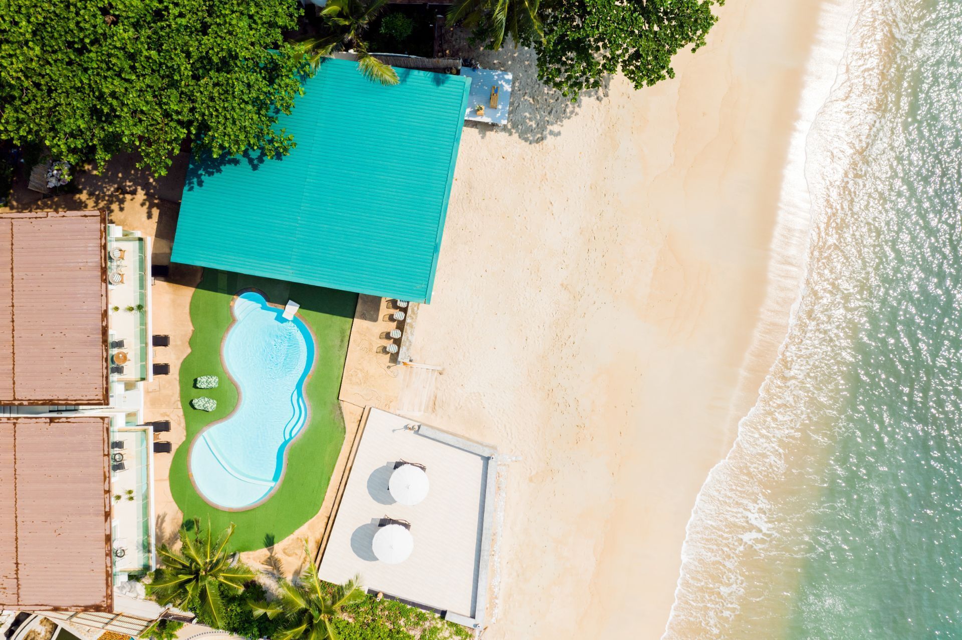 An aerial view of a beachside property with a swimming pool, a covered area, and a beach.