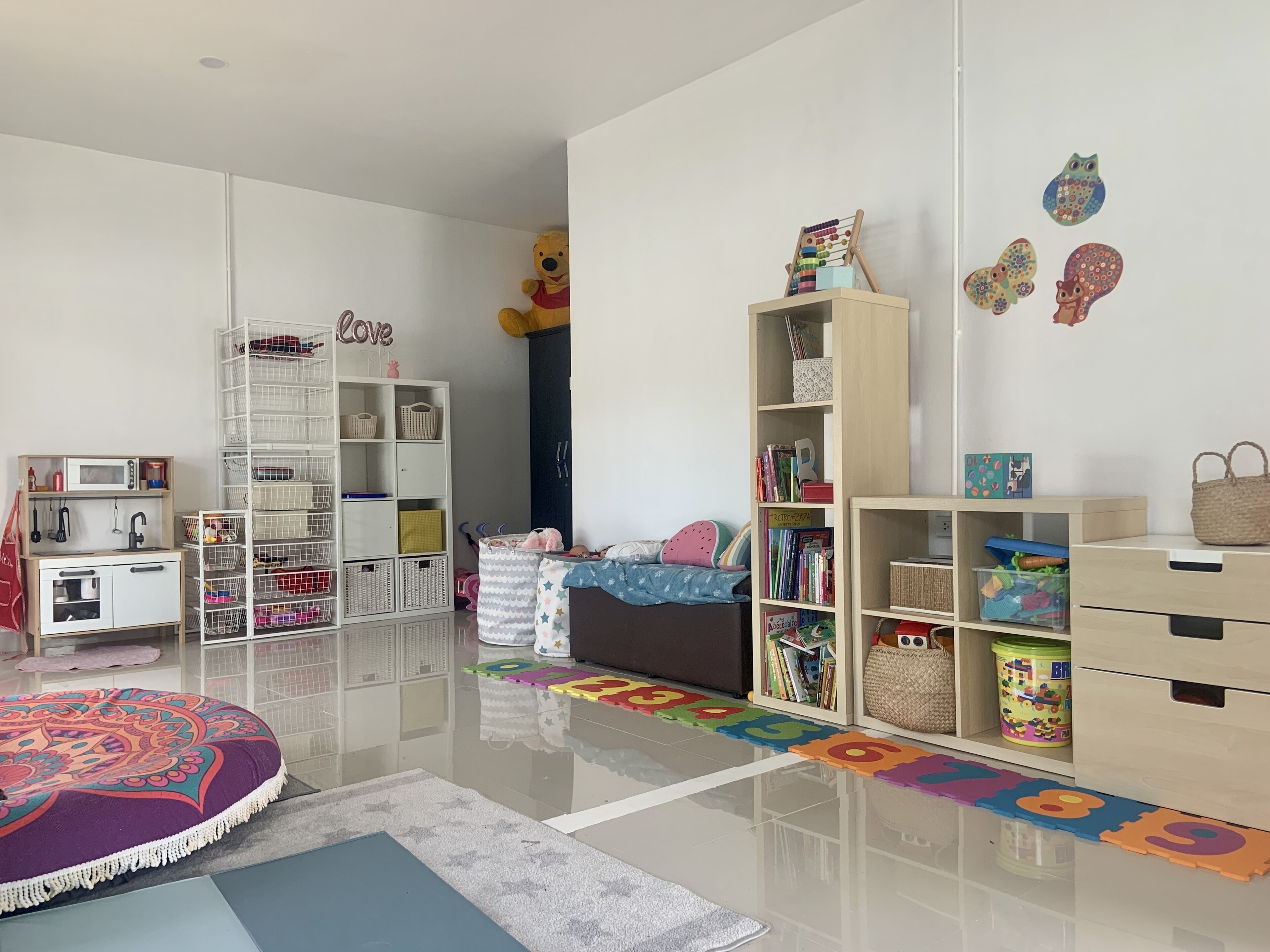 A child's playroom with a crib, shelving units, and a play mat.