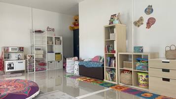 A child's playroom with a crib, shelving units, and a play mat.