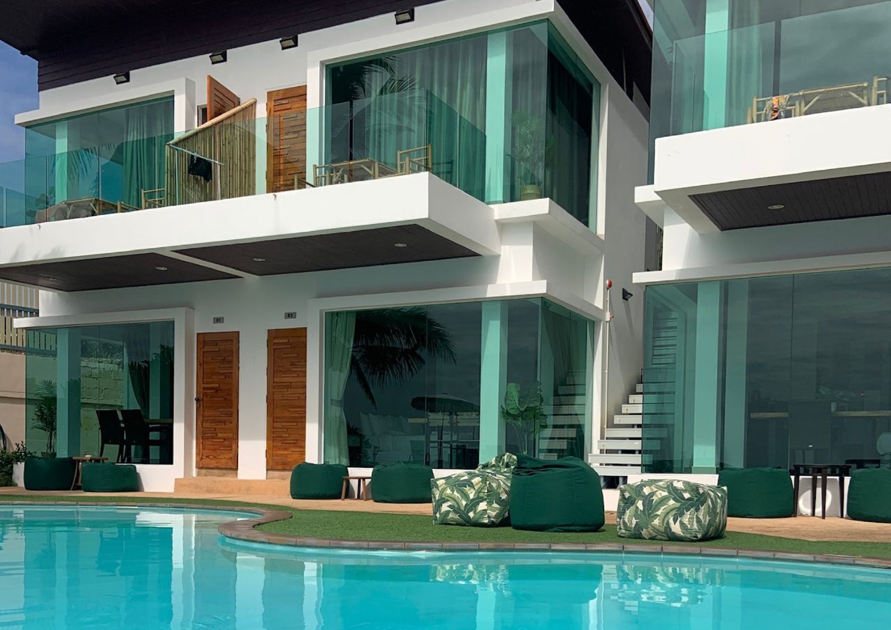 Une maison moderne à plusieurs étages, dotée d’une piscine, de grandes baies vitrées et d’un espace salon extérieur.